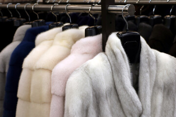 Fur coats in a row on a hanger in the store. Female fashion, natural mink fur clothes of different colors