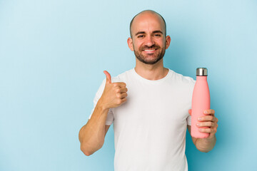 Young bald man holding canteen isolated on blue background  smiling and raising thumb up