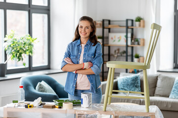 furniture restoration, diy and home improvement concept - happy smiling woman in gloves with crossed arms renovating old chair