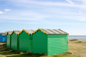 Fototapeta na wymiar bright green beach huts on the beach in Littlehampton England