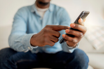 Cheerful businessman using smartphone while sitting on sofa at home. Closeup of mature black man using smartphone to checking email at home. Happy African american man using phone mobile at home.