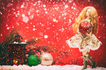 christmas ball in the hands of a doll on a red background and snow