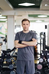 Fototapeta na wymiar Young muscular man resting in gym while looking at camera. Portrait of competitive sportsman at wellness center. Determined guy taking a break after working out session.