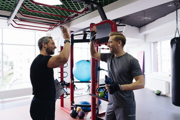 Fit man discussing workout plan with his trainer, personal coach before starting workout in the gym. Personal coach standing near young man give hi five