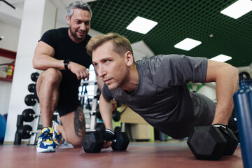 A personal trainer motivates the client to do push-ups in the gym. Personal workout hour with personal coach
