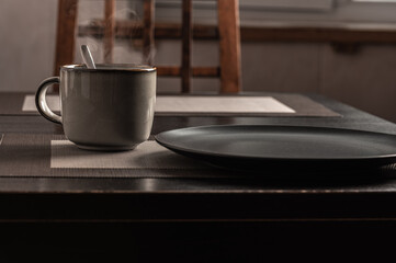 a cup of hot steaming tea on the table and an empty plate.