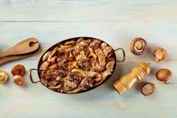 Beef stroganoff, mushroom and meat ragout in a creamy sauce, traditional Russian dish, in a skillet, shot from the top on a rustic wooden background