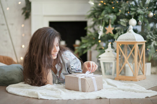 Beautiful young woman lying on the floor by the christmas tree with a gift box