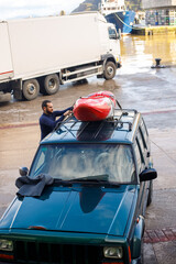 Young boy tying his kayak on top of the car hood to transport