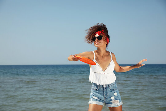 Happy African American woman throwing flying disk at beach on sunny day