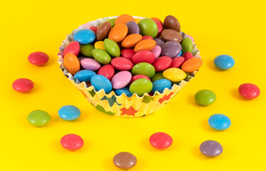 Colorful chocolate candy pills in bowl on yellow background