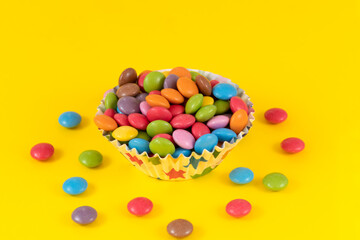 Colorful chocolate candy pills in bowl on yellow background