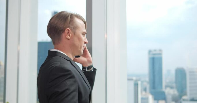 A Confident Businessman stading in office, Looking out of the window and making Important phone call with someone