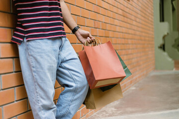 shopping concept A person in light blue jeans and white shoes leaning on the wall of the building while holding a lot of paper shopping bags