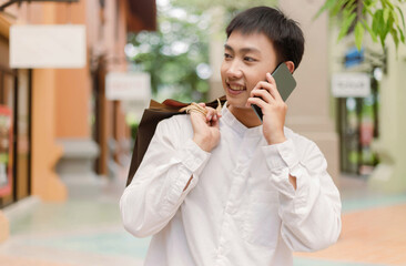 shopping concept The shopping man who puts shopping bags on his back giving his smile to the shop on his right while having a conversation with someone on the phone