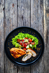 Stuffed chicken breast with mozzarella and fresh vegetable salad on wooden background
