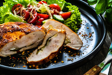 Stuffed chicken breast with mozzarella and fresh vegetable salad on wooden background
