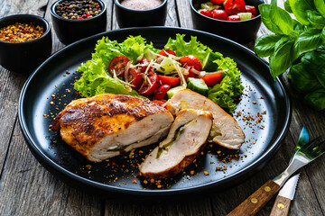 Stuffed chicken breast with mozzarella and fresh vegetable salad on wooden background
