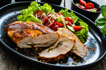 Stuffed chicken breast with mozzarella and fresh vegetable salad on wooden background
