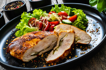 Stuffed chicken breast with mozzarella and fresh vegetable salad on wooden background

