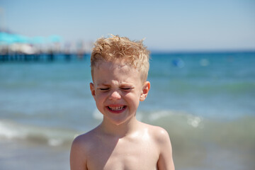 Portrait of a little boy crying on a beach on the seashore, he is upset. Concept summer vacation, rest, fun.