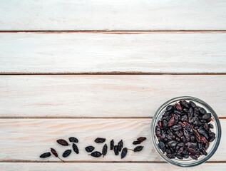 Dry barberries in a bowl on the background of white wooden boards.