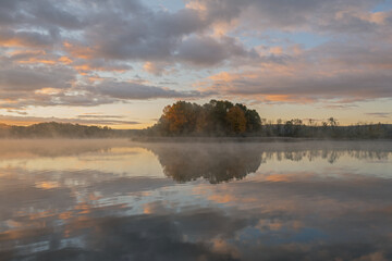 Foggy autumn landscape at dawn of the shoreline of Whitford Lake with mirrored reflections in calm water, Fort Custer State Park, Michigan, USA