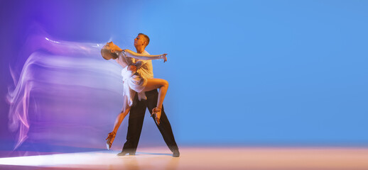 Young graceful dancers, flexible man and woman dancing ballroom dance isolated on gradient blue...