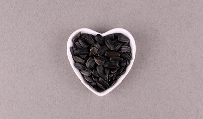Sunflower seeds in a white plate in the shape of a heart on a gray background