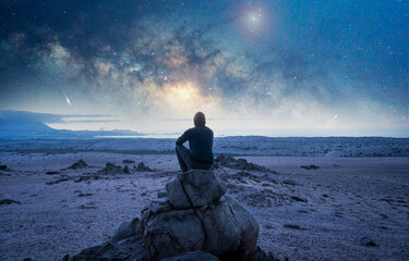 person on the rock outdoors meditating or praying at night under the Milky Way and shooting star
