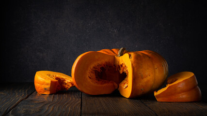 sliced pumpkin lies on a wooden table against the background of a dark gray wall with a spot of light. artistic moody still life in rustic style with copy space