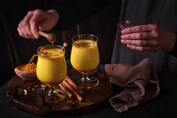 Gordijnen Turmeric golden milk latte with cinnamon sticks and honey. Healthy ayurvedic drink. Trendy Asian natural detox beverage with spices for vegans. Copy space. © kasia2003