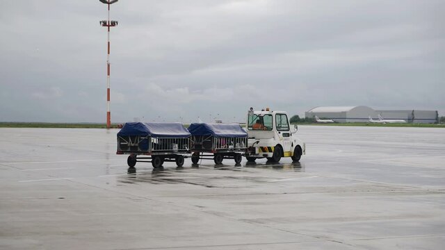 A tractor at the airport drags luggage carts along the runway. General plan shooting