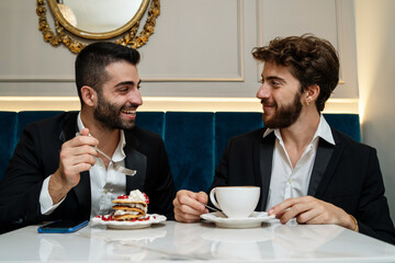 Two young colleagues dressing in suit discussing project together having a breakfast at restaurant cafe - business and food concept