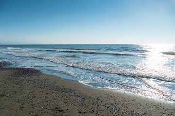 Sandy beach with pebbles, sea waves roll onto the beach on a sunny day