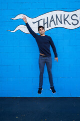 Portrait of the young man jumping against blue background with word thanks on it