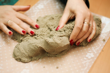 Closeup photo of female hands with newly painted red nails and kinetic sand. Sand therapy