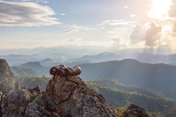 binoculars on top of rock mountain at beautiful sunset background.