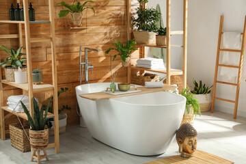 Stylish bathroom interior with white tub and green houseplants near wooden wall. Idea for design