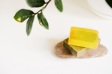 Handmade organic eco olive and lemon chamomile sea buckthorn soap on a natural stone stand. Simple minimalistic template with blurry leaves of zamiokulkas in a white pot on a neutral light background.