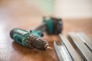 A dirty drill and new drywall profiles lies on a brown floor indoors