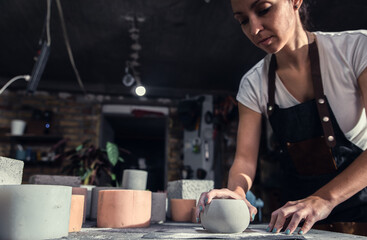 Craftswoman in apron working in her workshop making decorative concrete vase.	