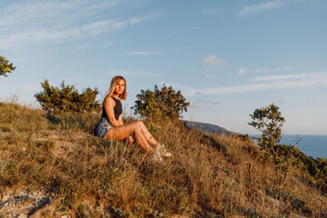 Attractive woman relaxing in nature with warm sunset. Young girl in coastline mountains