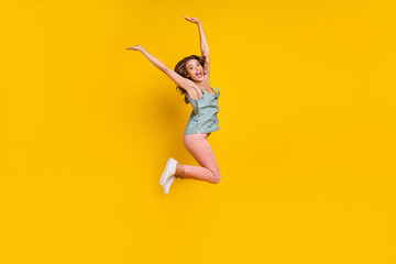 Full size photo of cheerful positive young woman jump up raise hands smile active isolated on yellow color background