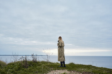 Obraz premium Girl stands on the edge of a cliff and looks at the ocean or sea. The woman looks into the distance. Amazing scenic nature view. Beautiful rocks and sea. Harmony, relaxing lifestyle. Travel, adventure