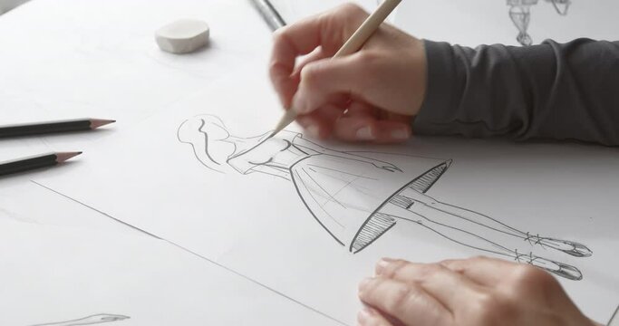 Fashion designer draws pencil sketches on paper of women's clothing.