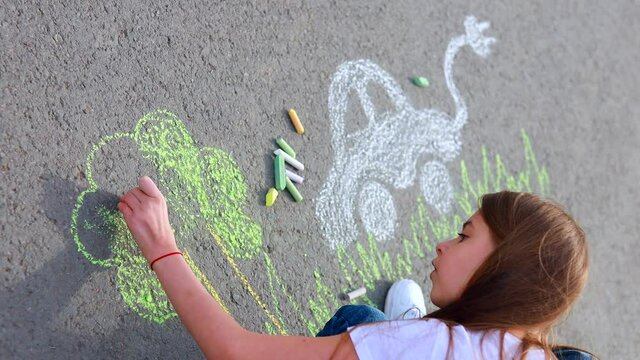 Little girl with creative craft hobby drawing electro on the asphalt with chalk car environment, eco friendly, save energy in park at summer day