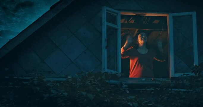 Happy Woman Waves To Someone From The Penthouse Of An Old House. It A Dark, Gloomy Night Outside