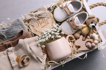 Wooden box with baby clothes, booties and toys on grey background, top view