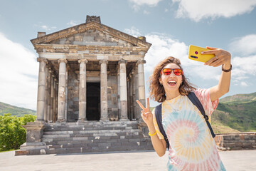 Happy female tourist takes a selfie photo against the background of the famous Garni Temple - one...